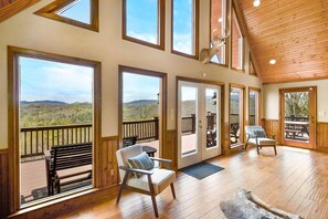 Ein geräumiges Zimmer mit großen Fenstern, einer Holzbalkendecke und Blick auf die Berge.