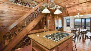 Ein Holzblockhaus-Interieur mit Kücheninsel, Essbereich und Treppe mit dekorativer Geländer.