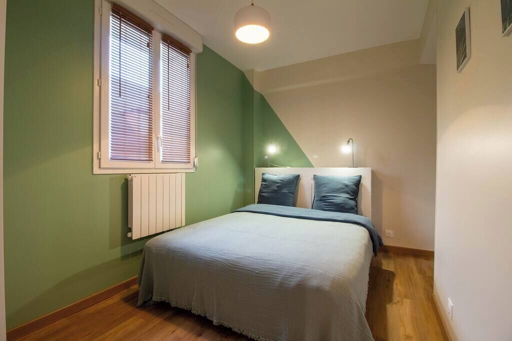 Ein Schlafzimmer mit Bett, Fenster mit Jalousien, Heizkörper und Deckenleuchte.