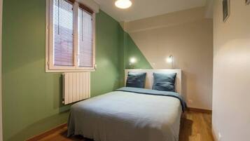 A bedroom with a bed, a window with blinds, a radiator, and a ceiling light.