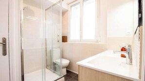 Ein modernes Badezimmer mit einer ein Glasfach raumseitig abgetrennten Dusche, einer weißen Toilette und einem weißen Waschbecken mit Spiegel.