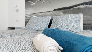 Ein Schlafzimmer mit Bett, ausgestattet mit gemusterten Betttextilien, Blick auf den Strand mit Möwen und einem ordentlich aufgerollten Handtuch.