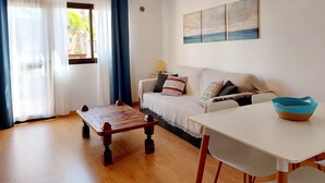 Ein Wohnzimmer mit einem Holztisch, einem weißen Sofa mit Kissen, einem weißen Tisch und einem blauen Korb.