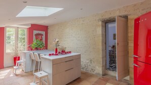 A modern kitchen with a central island, white bar stools, a red refrigerator, and a view through an open door. - DOMAINE DU MOULIN D'ANDRAUT Bordeaux-horses-golf-St Emilion (Saint-Sulpice-et-Cameyrac)