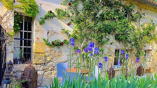 A rustic stone building with ivy and purple flowers, outdoor seating, and a lantern. - DOMAINE DU MOULIN D'ANDRAUT Bordeaux-horses-golf-St Emilion (Saint-Sulpice-et-Cameyrac)