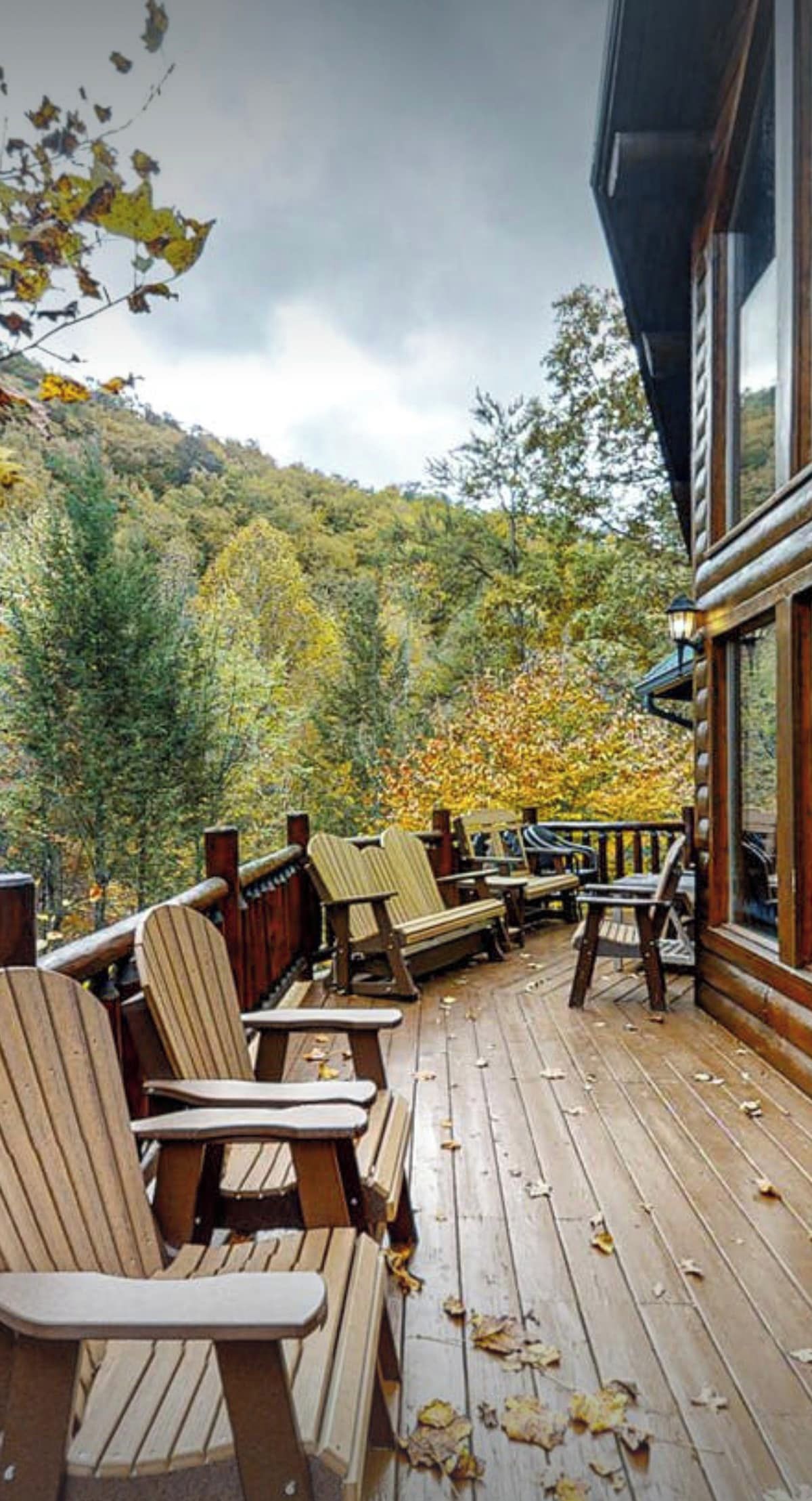 Puinen terassi, jossa on Adirondack-tyylisiä tuoleja ja penkki, ja jolta avautuu näkymä metsäiselle rinteelle.