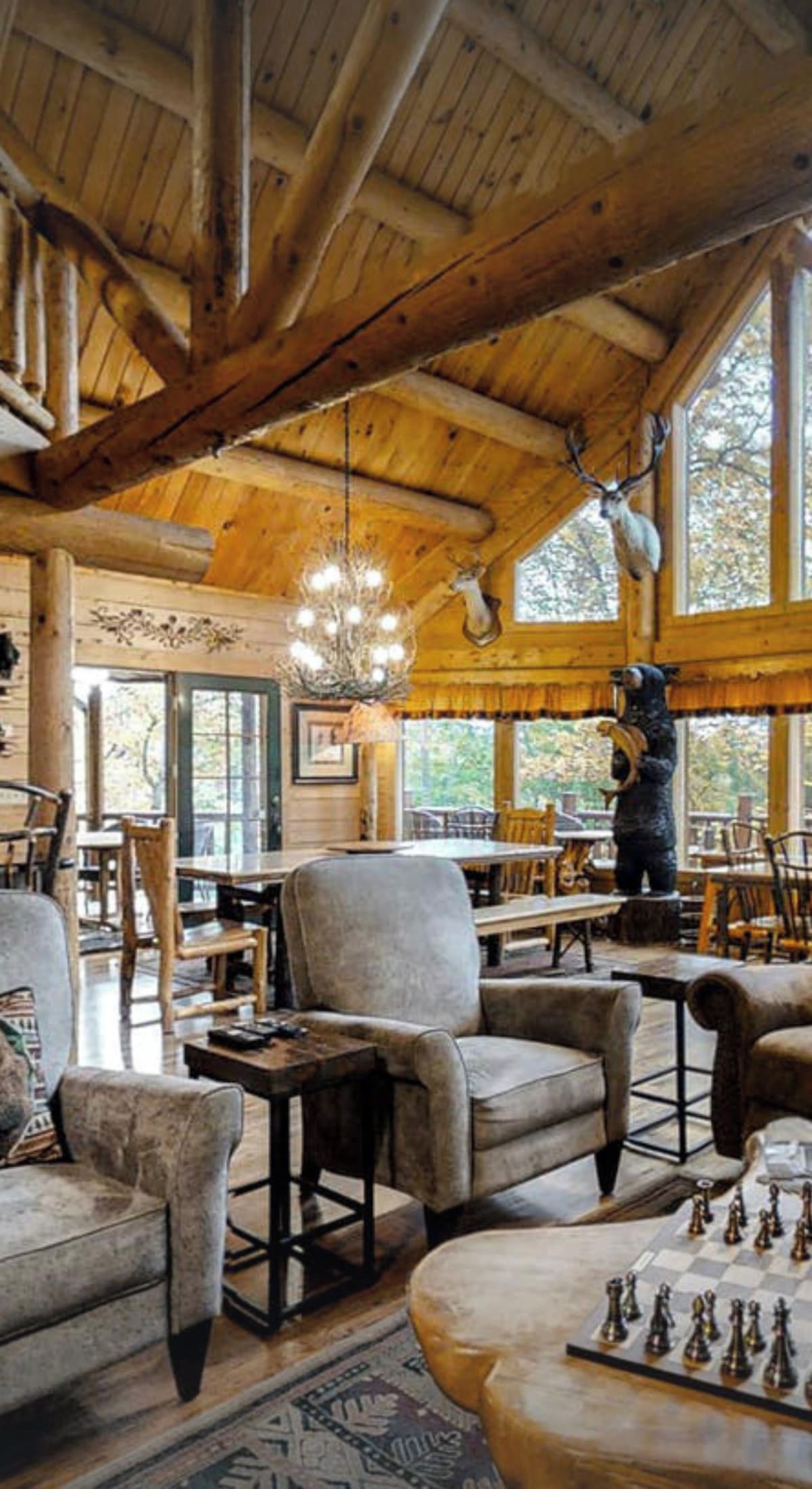 L’intérieur d’un chalet rustique, avec des poutres en bois, un lustre, une statue d’ours et un jeu d’échecs.