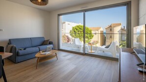 Een moderne woonkamer met een bank, salontafel en een grote schuifdeur naar een buiten zitgedeelte met witte stoelen en een tafel.