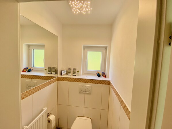 A small bathroom with a toilet, a sink, a mirror, and a window. - Weinberg Idyll vacation apartment - Fantastic view over vineyards to Lake Constance (Lindau)