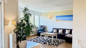 A living room with a sofa, a table, a lamp, a large potted plant, and a leopard print rug. - Weinberg Idyll vacation apartment - Fantastic view over vineyards to Lake Constance (Lindau)