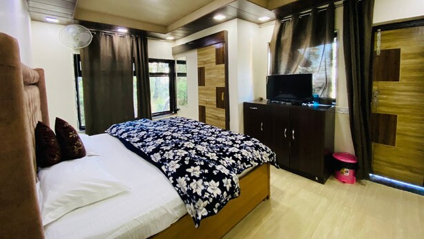 Une chambre à coucher avec un lit, un téléviseur posé sur un meuble en bois et une fenêtre avec des rideaux.
