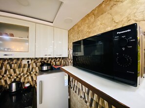 Une cuisine avec un réfrigérateur blanc, un four à micro-ondes et une cuisinière. Le mur derrière la cuisinière est recouvert d’un revêtement décoratif, et il y a un meuble blanc au-dessus de la cuisinière.