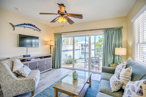 A living room with a ceiling fan, a flat-screen TV, a sofa, a coffee table, and a view of a pool and outdoor furniture. - Waterfront Retreat (Duck Key)