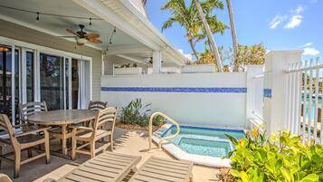 A poolside area with a dining table and chairs, a pool, and palm trees.
