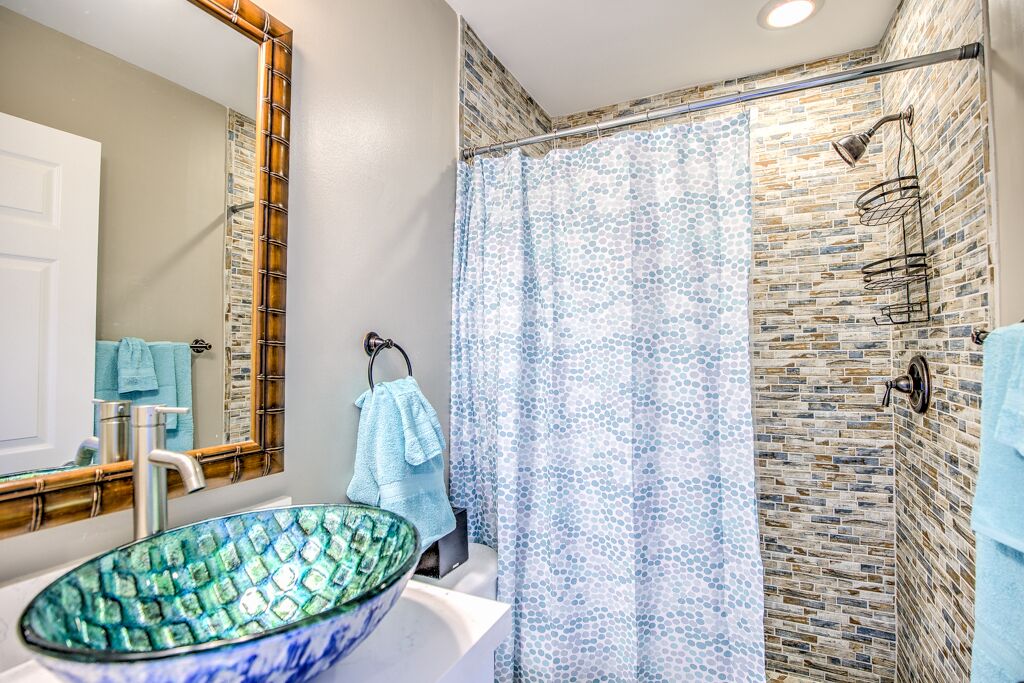A bathroom with a glass bowl sink, a shower with a patterned curtain, and a stone wall.