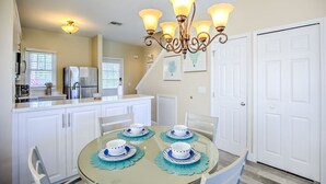 A dining area with a round table set for four, white cabinets, a refrigerator, and a chandelier. - Waterfront Retreat  (Duck Key)