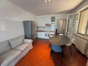 A compact living space with a kitchenette, a dining area with a round table and chairs, a sofa, and a window with blinds.