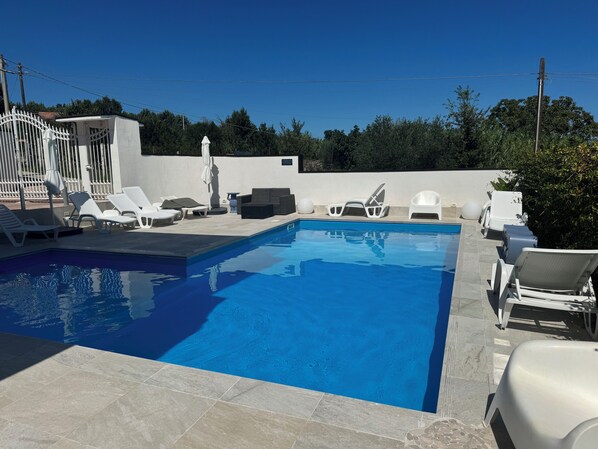 A swimming pool with lounge chairs and a white fence.