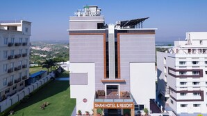 Un hotel moderno con entrada central, varios pisos y un área de estacionamiento.