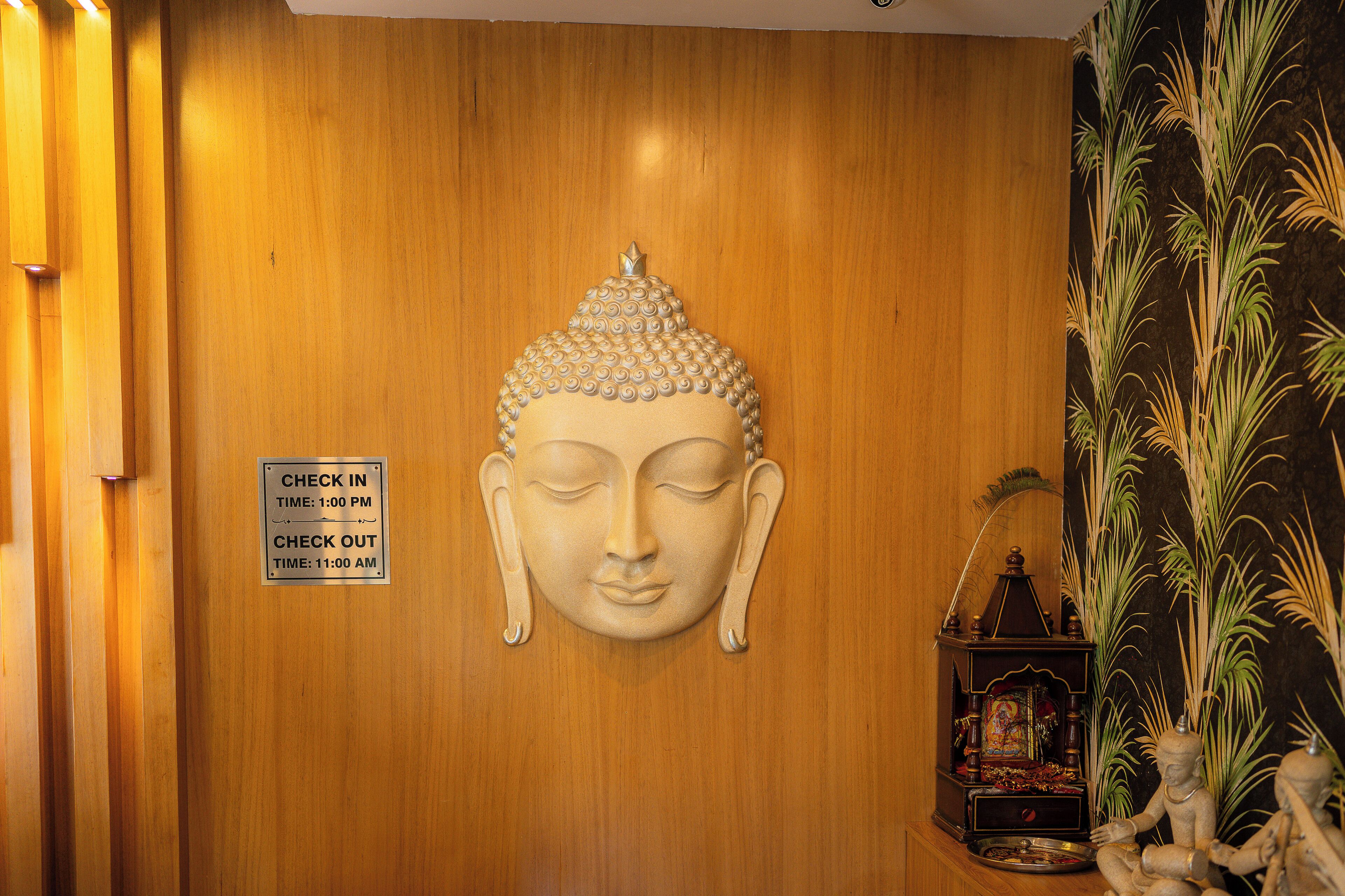 A wooden wall with a Buddha head sculpture and a check-in/out sign.