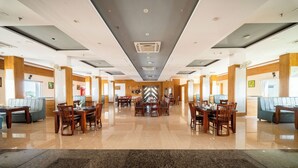 Un amplio vestíbulo de hotel con zona de comedor central, varios arreglos de asientos y un diseño moderno de techo.