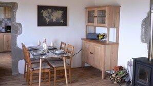 Zona pranzo con tavolo in vetro, sedie di legno, una mappa del mondo appesa al muro, pensili in legno e stufa a legna.