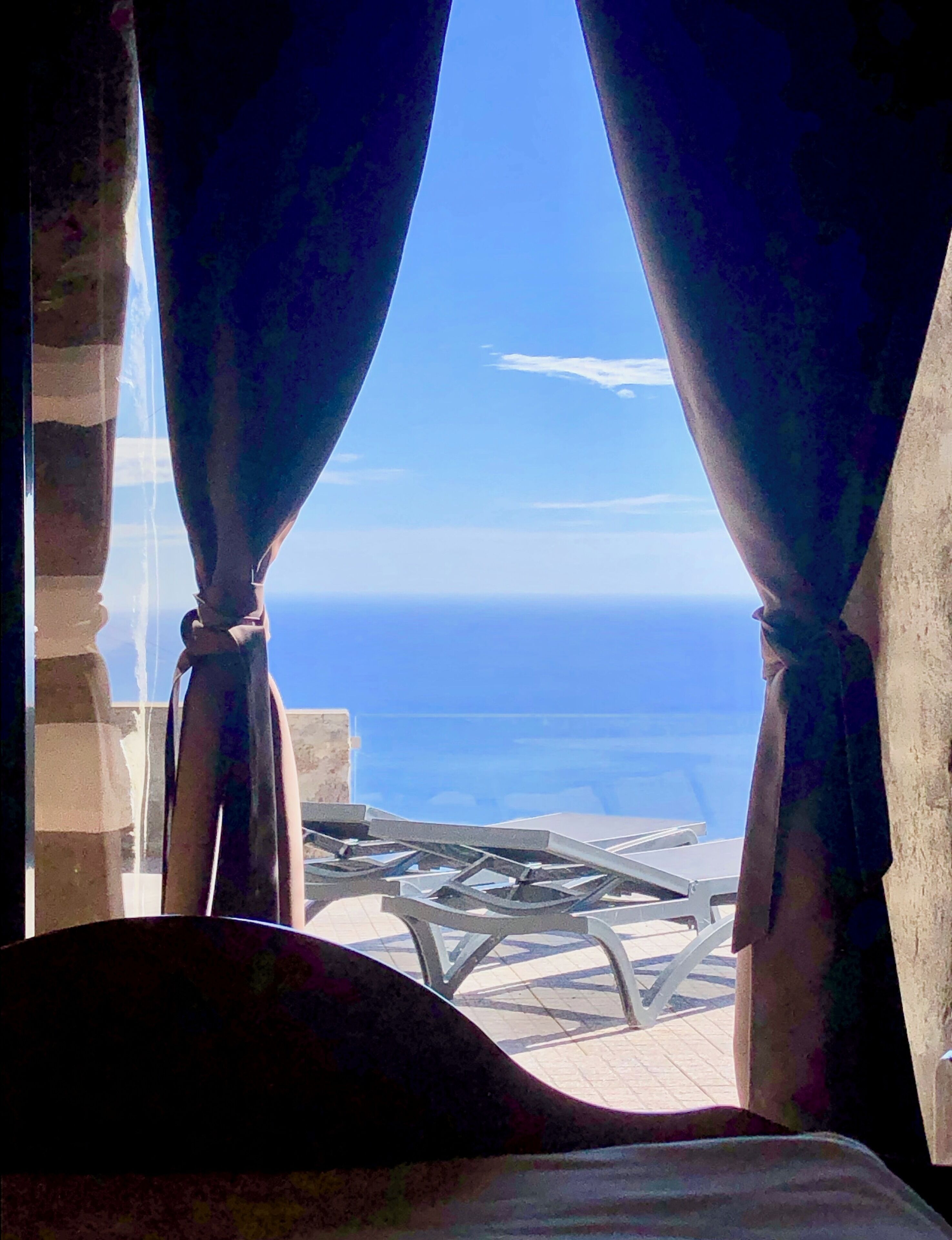 A room with a view of the sea through curtains, a bed, and a table with chairs.