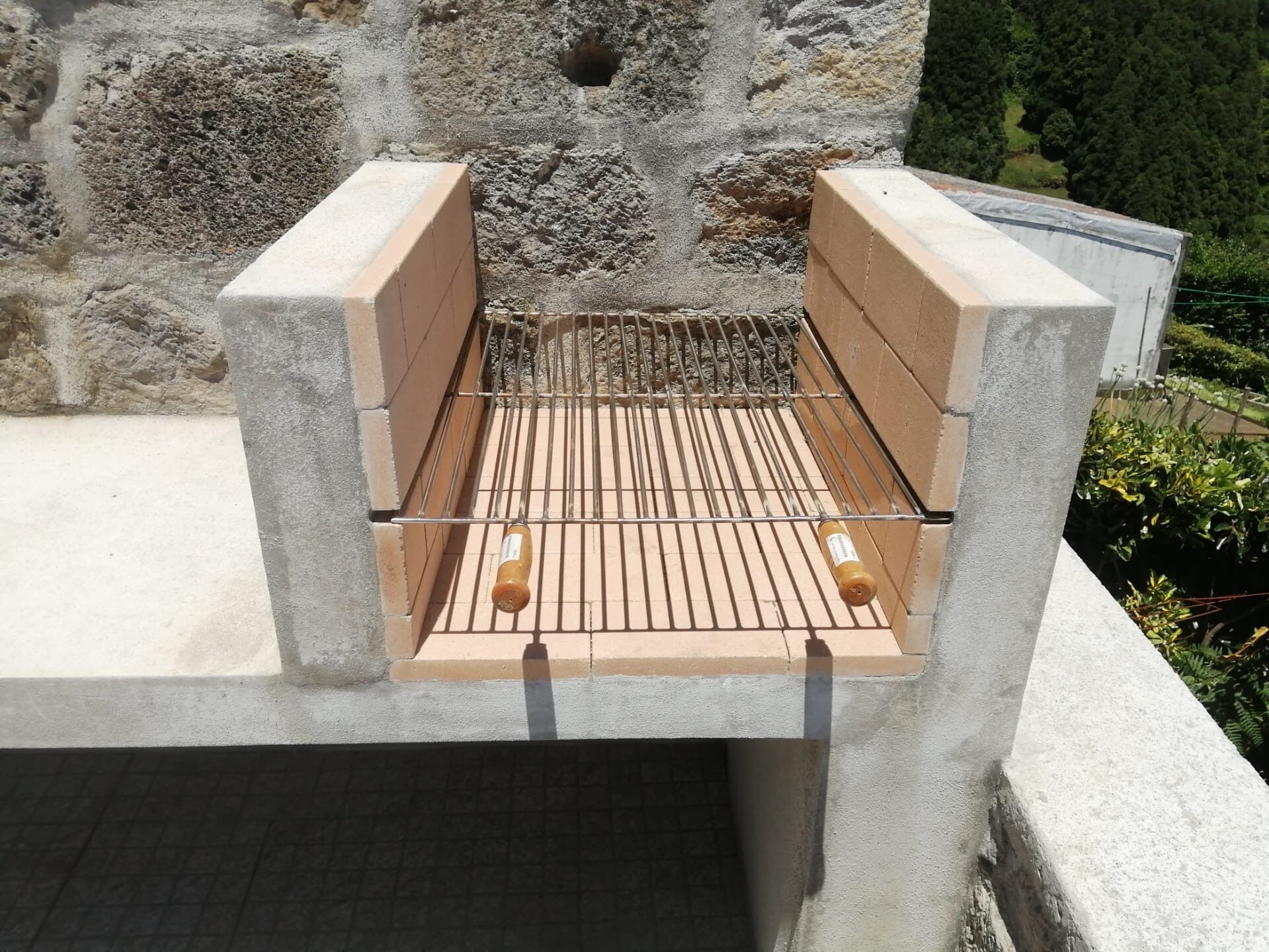 A concrete barbecue grill with a metal grate and two bottles of barbecue sauce.