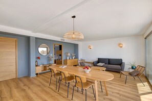 A modern living room with a wooden dining table, sofas, and a large window.