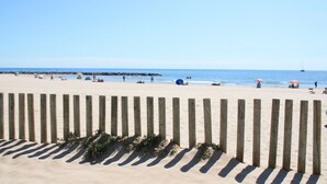 Une plage de sable bordée de barrières en bois, sous un ciel bleu et dégagé.