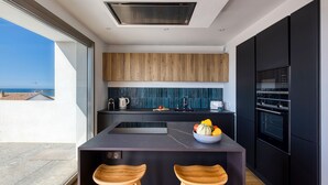 Une cuisine moderne dotée d’un grand îlot central, de meubles de rangement aux couleurs sombres et offrant une vue sur la mer.
