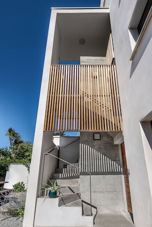 Un bâtiment moderne doté d’un escalier en béton, d’un balcon en bois à lattes et d’une plante en pot sur le palier.