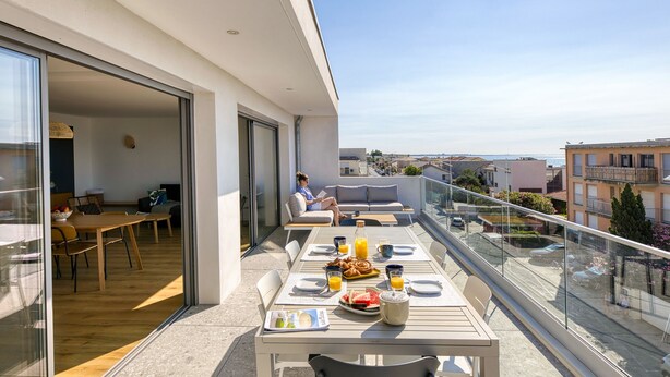 Un balcon avec une table à manger préparée pour le petit-déjeuner, un canapé et une personne qui lit.
