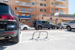 A parking lot with multiple cars, a building with balconies, and a no parking sign.