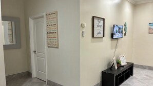 Um corredor com uma porta branca, um mural com uma mensagem motivacional, uma moldura com uma frase inspiradora e uma televisão sobre um suporte.