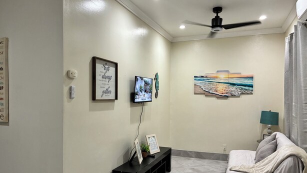 Uma sala de estar moderna com televisão de tela plana, ventilador de teto, um quadro e um sofá.