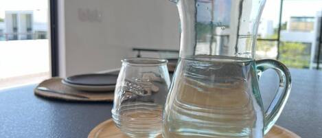A clear glass pitcher and a smaller glass on a wooden coaster on a dark countertop.