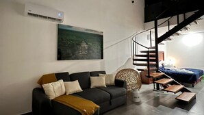 A modern living room with a sofa, a large painting, an air conditioning unit, and a staircase leading to an upper level. - Cozy loft with private jacuzzi. (Mérida)
