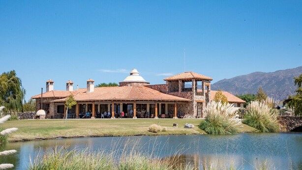 A large, historic building with a central dome and multiple chimneys, surrounded by a lake and mountains in the background. - Tranquilo! (Cafayate)