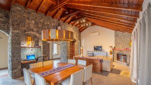 A spacious dining area with a wooden table and chairs, a stone wall, and a fireplace. - Tranquilo! (Cafayate)