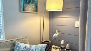 A room with a grey sofa, a starfish pillow, a lamp, a wall-mounted painting, and a small table with decorative items. - Ocean View Condo, Pool, Steps to Beach, Bikes & Beach Chairs Included (Ocean Isle Beach)