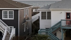 A beachfront property with a dark-colored house, a white house, and a turquoise staircase. - Ocean View Condo, Pool, Steps to Beach, Bikes & Beach Chairs Included (Ocean Isle Beach)