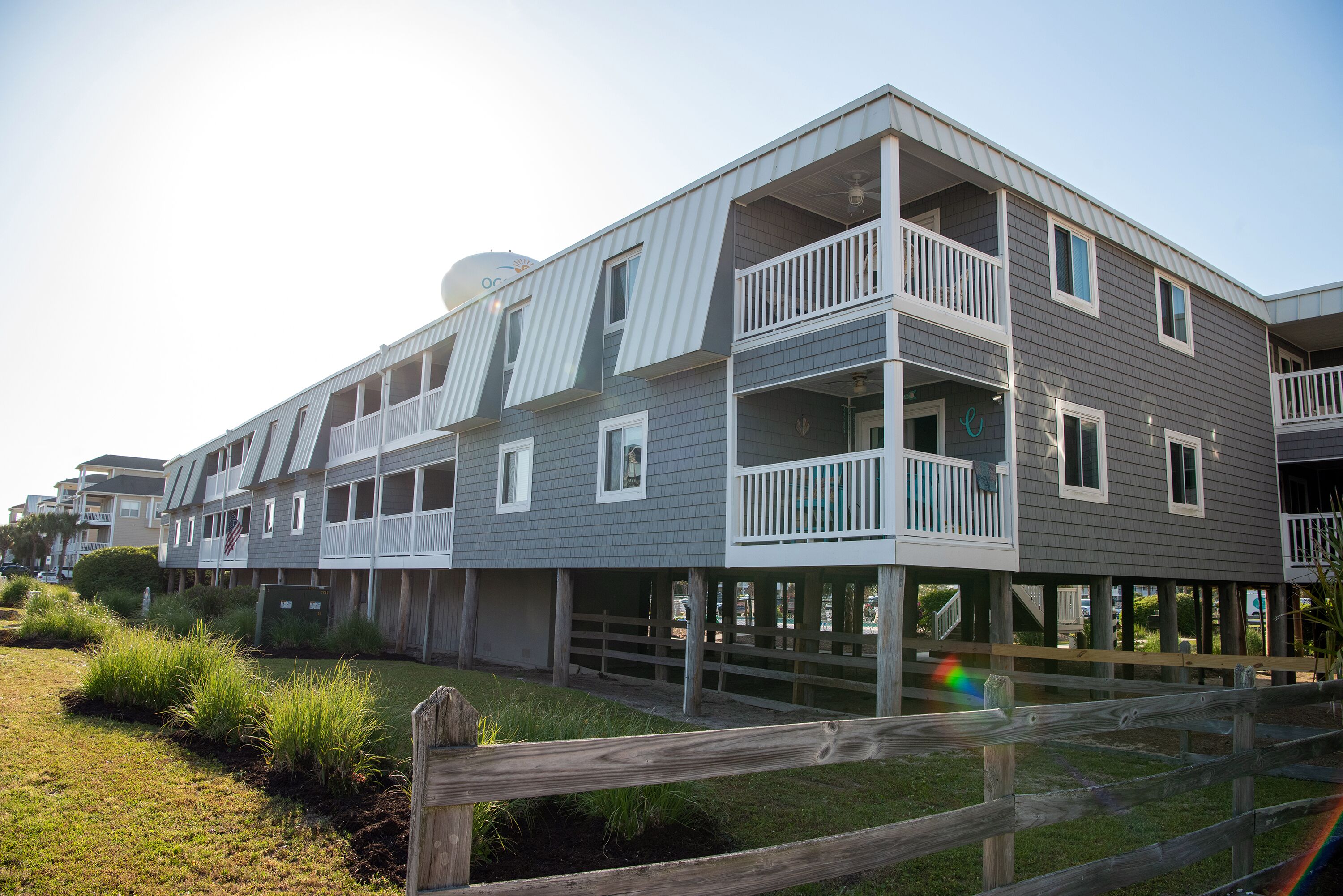 A multi-story building with balconies, a wooden fence, and a grassy area.