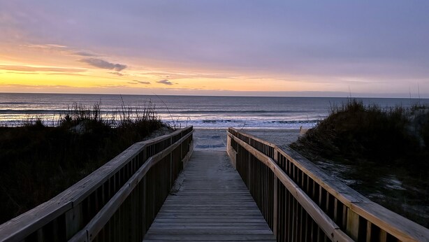 A wooden boardwalk leading to the ocean with a sunset in the background. - Ocean View Condo, Pool, Steps to Beach, Bikes & Beach Chairs Included (Ocean Isle Beach)