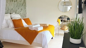 A bedroom with a bed, bedside table, and a potted plant. - Cosy (Apt7) - Patio, Sea View and pool (indigo Bay)