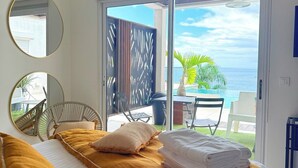 A bedroom with a bed, two round mirrors, a view of the ocean, and a balcony with outdoor furniture. - Cosy (Apt7) - Patio, Sea View and pool (indigo Bay)