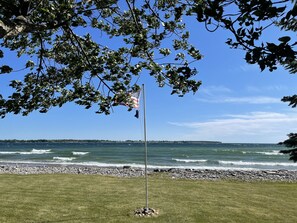 A grassy area with a flagpole, a rocky shoreline, and a view of the ocean.