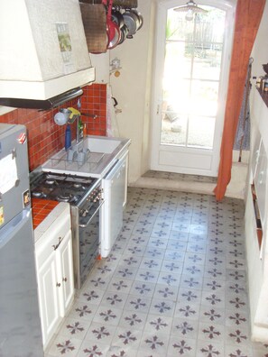 A kitchen with a stove, sink, and tiled floor.