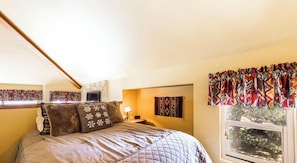 A bedroom with a large bed, a window with curtains, a stone wall, and a lamp.