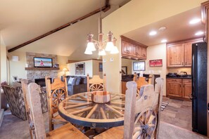 A dining area with a round wooden table and chairs, a stone fireplace, and a television mounted on the wall.